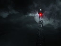 A radio mast is surrounded by darkness and clouds. A single red light glows.