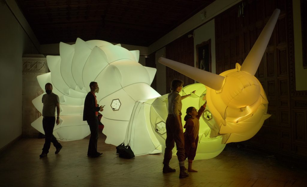 A large inflatable snail, lit from within with a young child reaching up to touch it.